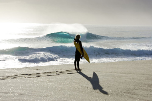 A surfer watching beautiful waves rolling in to the beach on King Island, Tasmania.